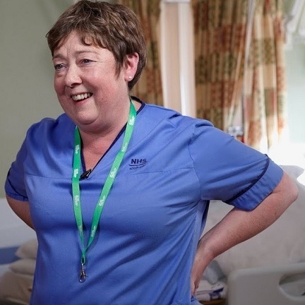 A smiling Macmillan healthcare professional wearing blue scrubs.